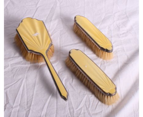 A silver and yellow enamel backed hairbrush and a pair of matching clothes brushes