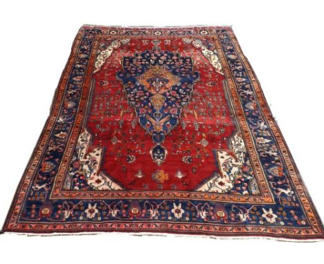 A Persian carpet, hand knotted with a red ground, the central asymmetrical medallion with pendant, 390 by 290cm.