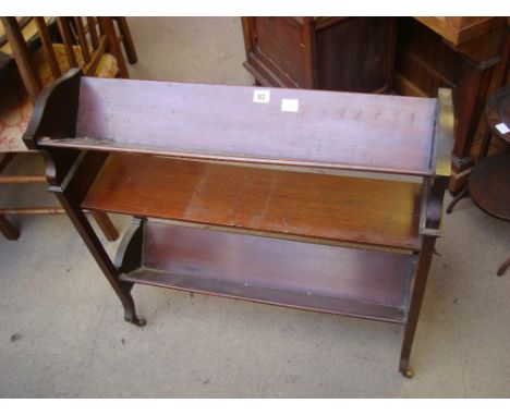 An Edwardian mahogany freestanding three tier book trough, on brass casters, (one trough with crack).