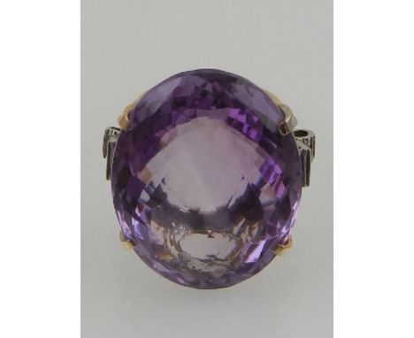 A 14 carat yellow gold and amethyst cocktail ring, the large faceted oval cut amethyst flanked by small diamond accents. 