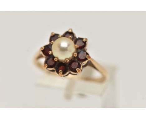 A YELLOW METAL PEARL AND GARNET CLUSTER RING, centring on a single cultured pearl claw set within a surround of circular cut 