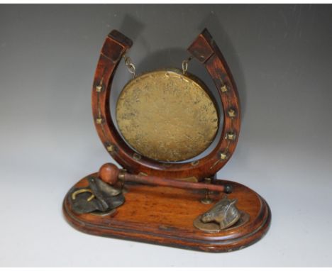 AN EQUESTRIAN THEMED HORSESHOE TABLE GONG, the gilt circular gong mounted on carved horseshoe, raised on a wooden plinth with