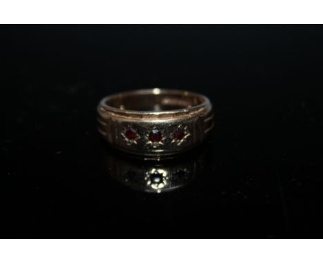 A HALLMARKED 9 CARAT THREE STONE RUBY RING, set in a wide band measuring 9 mm, approx weight 7.9g, ring size W