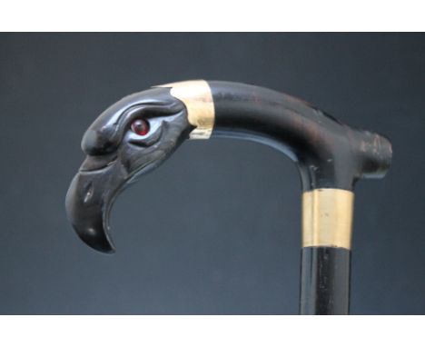 A VICTORIAN EBONISED WALKING STICK WITH CARVED HORN HANDLE IN THE FORM OF AN EAGLES HEAD, with inset glass eyes, gilt metal c