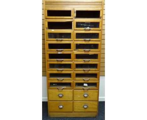 A late twentieth century light wood retailer's haberdashery cabinet with two columns of eight glazed drawers above four non-g