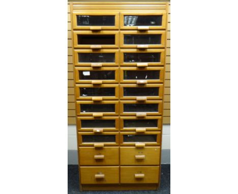 A late twentieth century light wood retailer's haberdashery cabinet with two columns of eight glazed drawers above four non-g