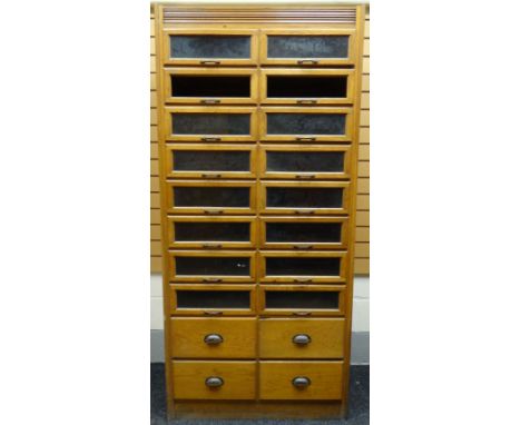 A mid-twentieth century light-oak retailer's haberdashery cabinet with two columns of eight glazed drawers above four non-gla