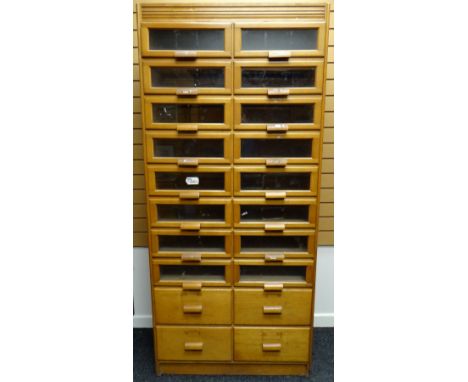 A late twentieth century light wood retailer's haberdashery cabinet with two columns of eight glazed drawers above four non-g