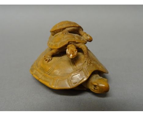A Japanese wood netsuke of a tortoise and young, inlaid eyes to the adult and one of the young, signed, 4.5cm. length.