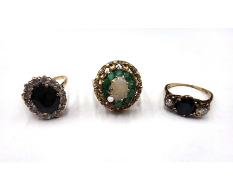 A 9ct gold, opal and emerald set oval cluster ring, (one emerald lacking), a 9ct gold, sapphire and diamond set three stone r