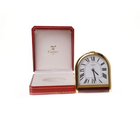 CARTIER TRAVELLING TIMEPIECEnumbered 10239, of arched form, gilt metal surround with burgundy strip to base, white enamel fac