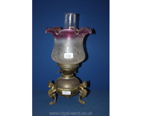 A Brass Oil Lamp standing on three legs formed as mythical sea creatures and having a cranberry tipped shade