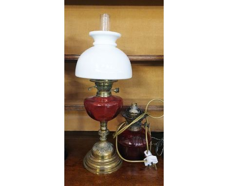 Oil lamp with cranberry glass-coloured well, on a stepped brass base, with a white opaque glass shade and another oil lamp co