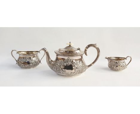 George V silver tea service comprising teapot with ivory finial, scrolling foliate embossed body, sugar pot and milk jug with