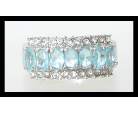 A white metal stamped 10k dress ring having central line of blue faceted stones flanked by two rows of prong set white stones