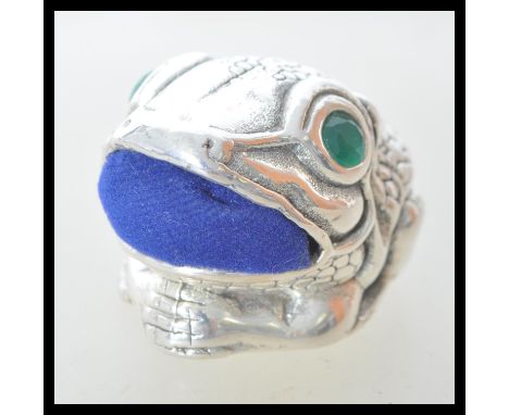 A stamped 925 silver pin cushion in the form of a toad having a blue fabric cushion to the mouth, set with faceted green emer