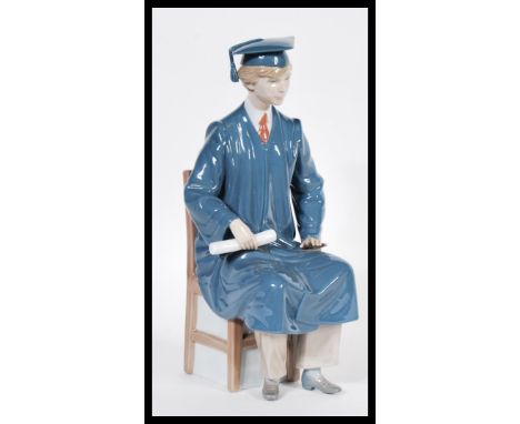 A Lladro ceramic figurine entitled the Graduate model 5198 in the form of a male student in graduation robes seated on chair.