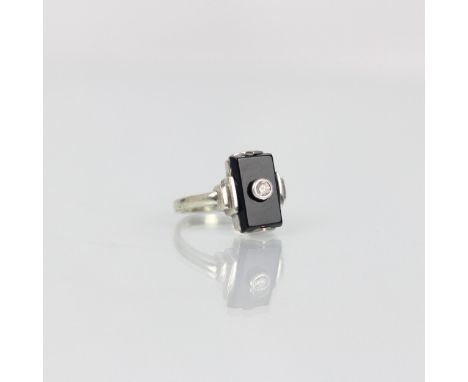 An Art Deco style 9ct white gold diamond ring, the central round cut diamond within white gold rubover mount upon onyx colour