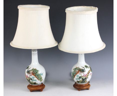 A pair of contemporary Chinese porcelain lamp bases, each decorated with a peacock among prunus blossom, on wooden stands, wi