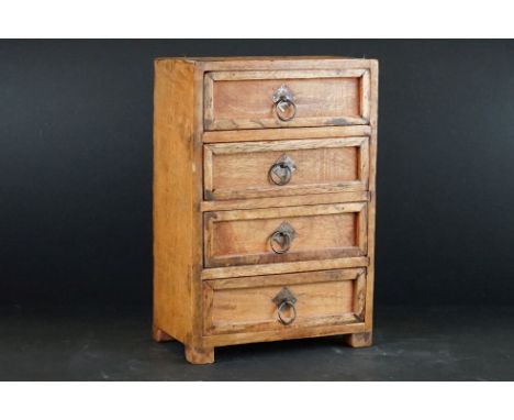 A wooden table top chest of four drawers with ring handles. 