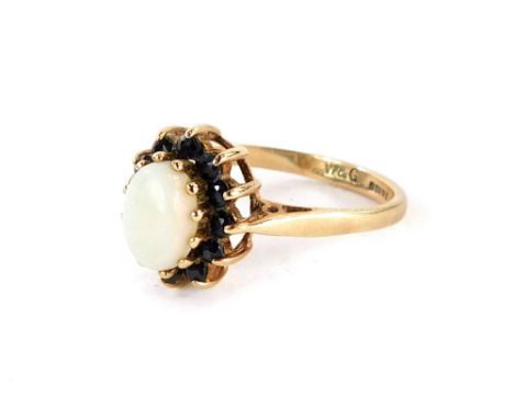 A 9ct gold dress ring, the central cluster with oval opal surrounded by dark blue round brilliant cut stones, in a raised bas