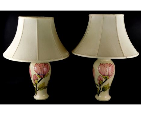 A pair of Moorcroft Magnolia pattern lamp bases, each decorated with pink flowers on a cream ground, with cream shades, 38cm 