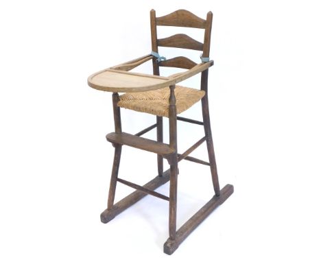 An early 20thC country made oak and ash ladder back child's high chair, with a rush seat on turned supports.