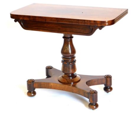 A William IV rosewood card table, the D shaped top above a scroll carved panelled frieze on a turned baluster and lotus carve