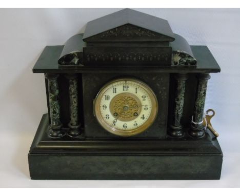 A slate mantle clock with marble columns. Either side of the dial displaying Arabic numbers.