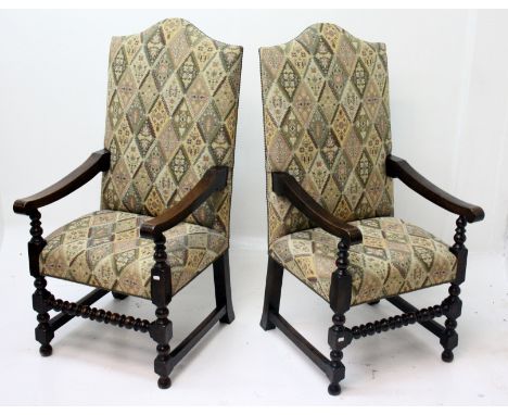 A pair of Cromwellian style oak open armchairs, each with an arched padded back and seat above a bobbin turned front stretche