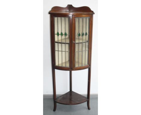 An Edwardian inlaid mahogany bow front standing corner cupboard, with a pair of lead lined, stained glass doors enclosing two