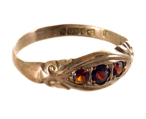 A 9ct gold and garnet three stone ring, the three graduated round cut garnets set in the 9ct gold band, having raised swag de