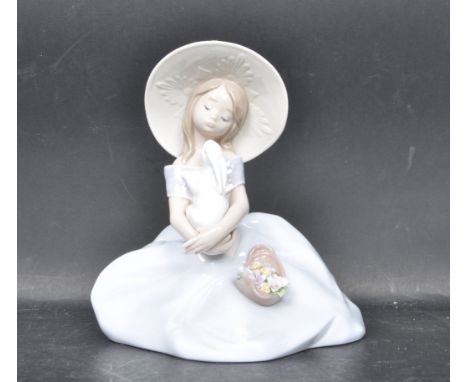 A ceramic porcelain Spanish Lladro figure entitled 'Bunny Kisses' depicting a girl seated and holding a white rabbit. Figurin