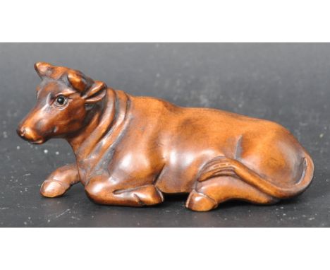 A Japanese oriental hand carved&nbsp;netsuke in a shape of a cow / water buffalo posing in sitting position with glass eyes a
