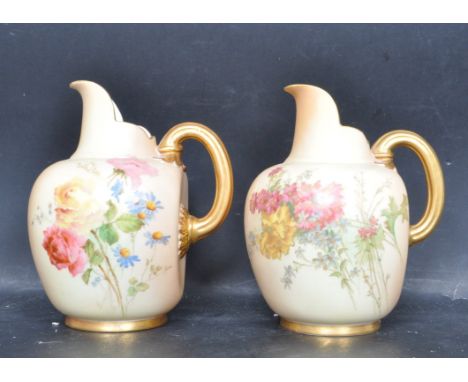 A pair of large early 20th century Royal Worcester blush ivory flat back jugs being decorated with floral sprays, gilded hand