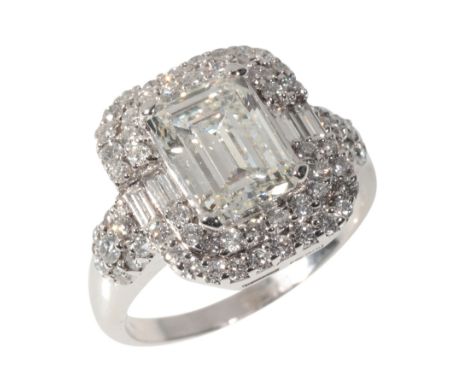 AN EMERALD CUT DIAMOND CLUSTER RINGin 18ct white gold, set with an emerald-cut diamond of c.3.10 carats held in a four-claw s