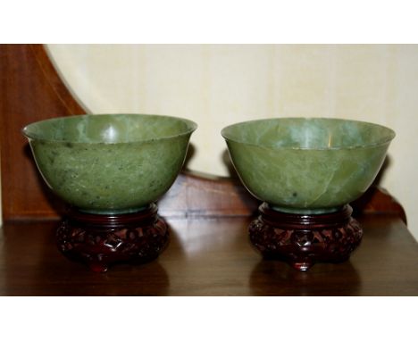 A pair of Chinese carved pale green jade bowls, late 20th century, on hardwood stands. (4)