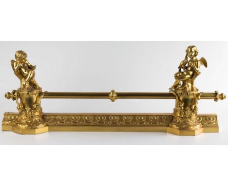 A gilt brass Empire style fire fender, the top horizontal tubular rail with centralised ring, flanked by two cherubs on cylin