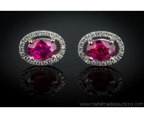 A pair of 18ct white gold, ruby and diamond 'halo' earrings, the two oval cut rubies of good colour, total weight 1.80 carats
