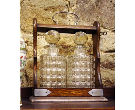 An oak two bottle tantalus, early 20th century, with plated mounts and two cut glass decanters with globe stoppers, with key,