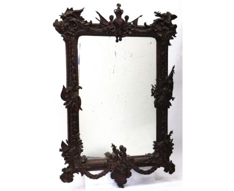 AN EASTERN CARVED HARDWOOD FRAMED WALL MIRROR with a crown finial crest, adorned with dragons, suits of armour and scrolling 