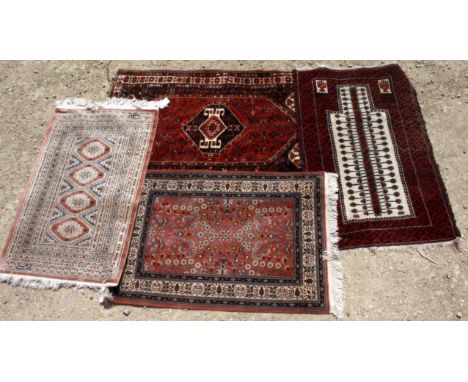 FOUR 20TH CENTURY CARPET RUGS, two on red ground, one on a plum ground and one with cream and ivory ground, all with geometri