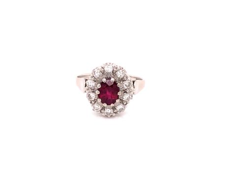 AN 18ct WHITE GOLD RUBY AND DIAMOND CLUSTER RING. THE OVAL CLAW SET RUBY SURROUNDED BY A CLUSTER OF DIAMONDS. FINGERS SIZE R,