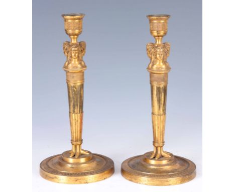 A STYLISH PAIR OF EARLY 19TH CENTURY GILT BRASS FRENCH CANDLESTICKS with mask head and engine turned tapering stems terminati