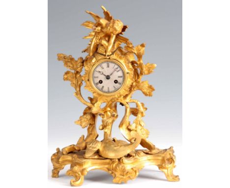 AN EARLY 19th CENTURY MINIATURE ROCOCO ORMOLU MANTEL CLOCK modelled as Cupid firing an arrow at a mythical winged creature wi