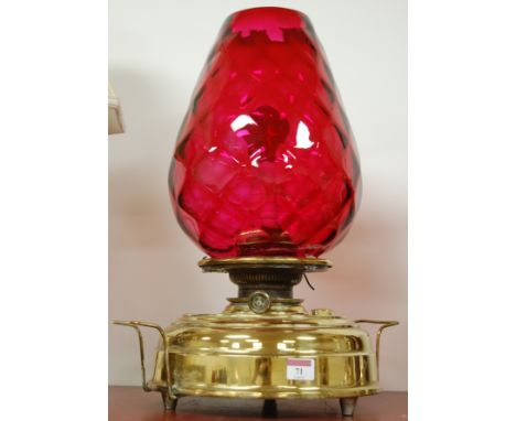 An early 20th century brass oil lamp having circular twin handled base and conical ruby glass shade (converted for electricit