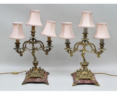 A PAIR OF CONTINENTAL BRASS THREE-LIGHT TABLE LAMPS, having decorative twin branch form with cast putti stems and rouge marbl