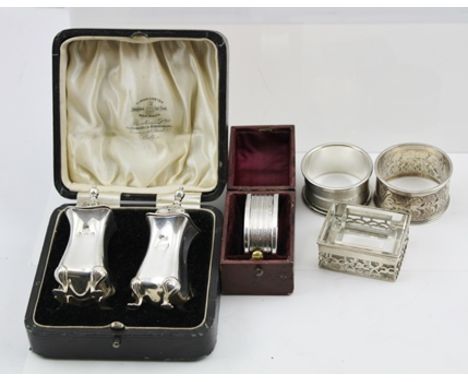 THREE SILVER NAPKIN RINGS, one in a silk and velvet lined case, a PAIR OF SILVER CONDIMENTS, cased, and a silver mounted STAM