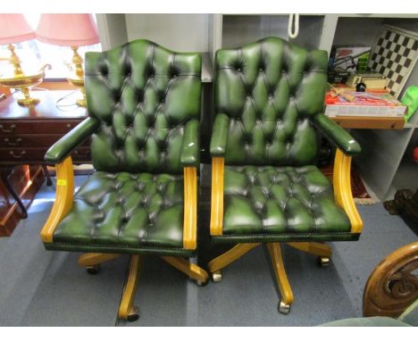 Two green leather button back office open armchairs, lightwood framed on swivel bases and castors 