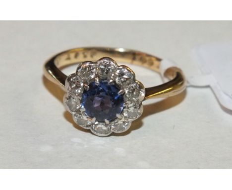 A sapphire and diamond cluster ring set round-cut sapphire of pale blue within a surround of ten brilliant-cut diamonds, in 1